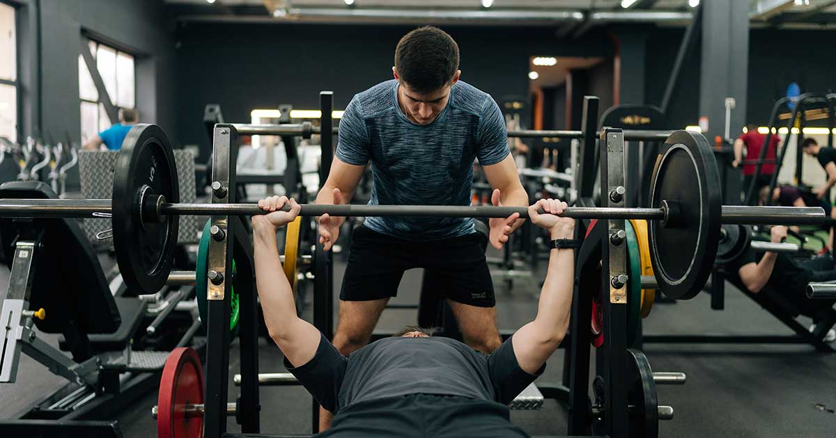 Athlet führt Bankdrücken mit Spotter im Fitnessstudio aus – typische Push-Übung im Push-Pull-Legs-Trainingsplan.